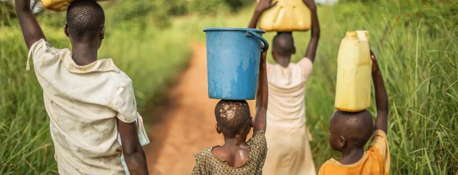 Group of young African kids walking with buckets and jerrycans on their head as they prepare to bring clean water back to their village.