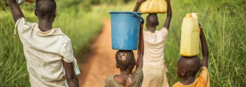 Group of young African kids walking with buckets and jerrycans on their head as they prepare to bring clean water back to their village.