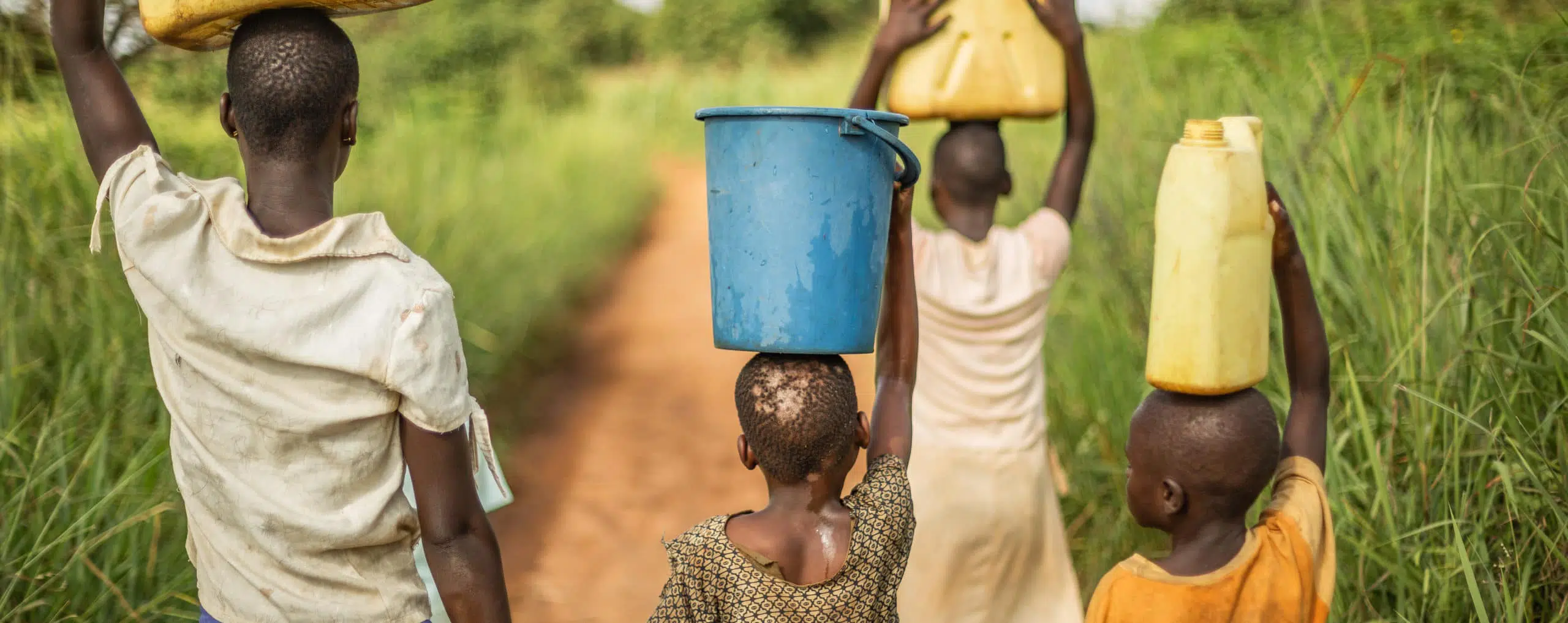 Group of young African kids walking with buckets and jerrycans on their head as they prepare to bring clean water back to their village.