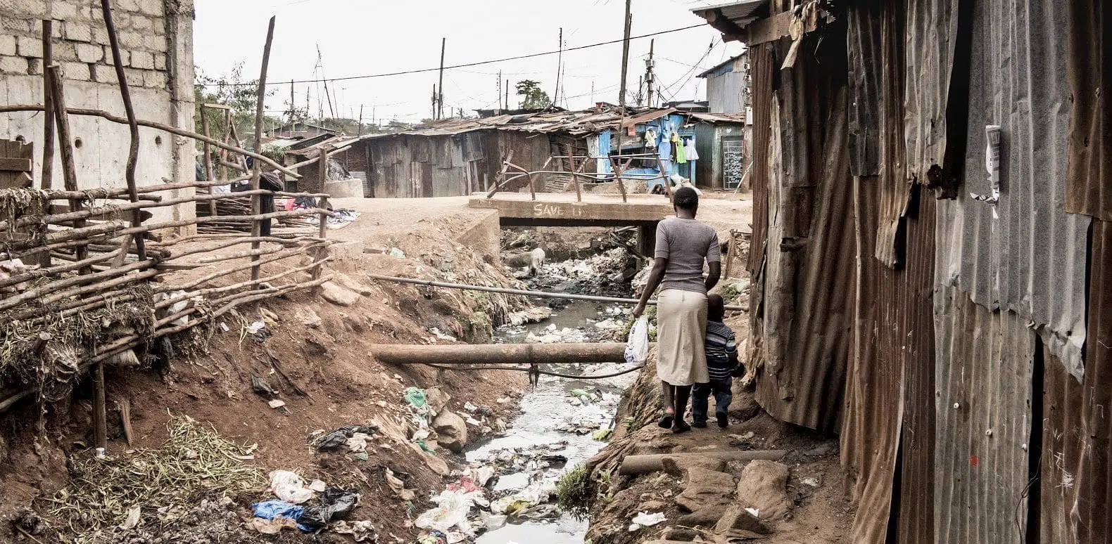 People walking along an open sewer in a slum in Africa