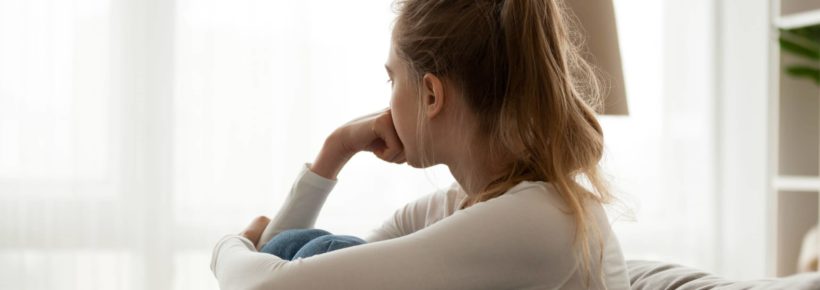 Upset woman sitting on couch alone at home woman sad pensive looking out window