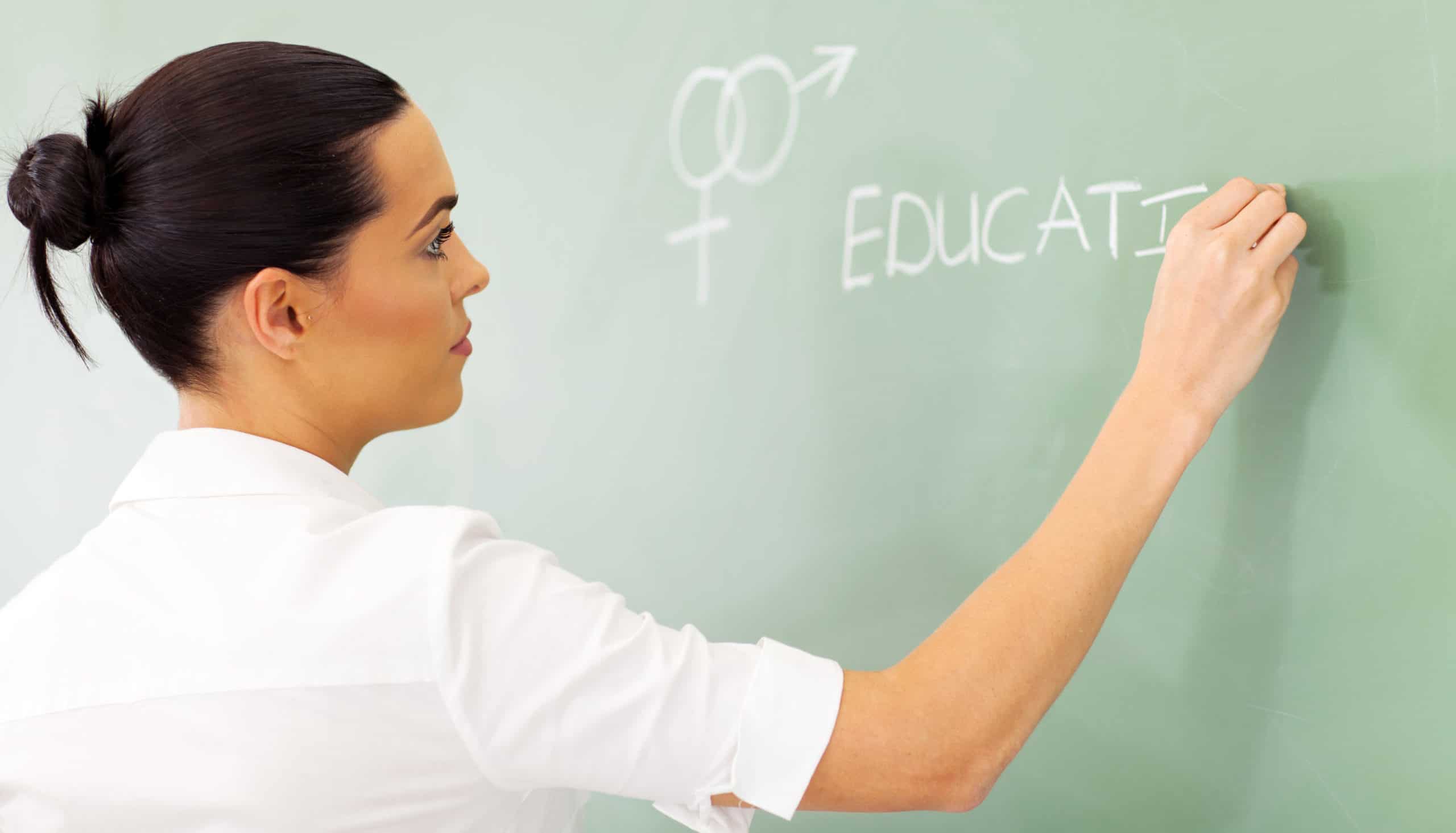 female high school educator writing sex education on chalkboard
