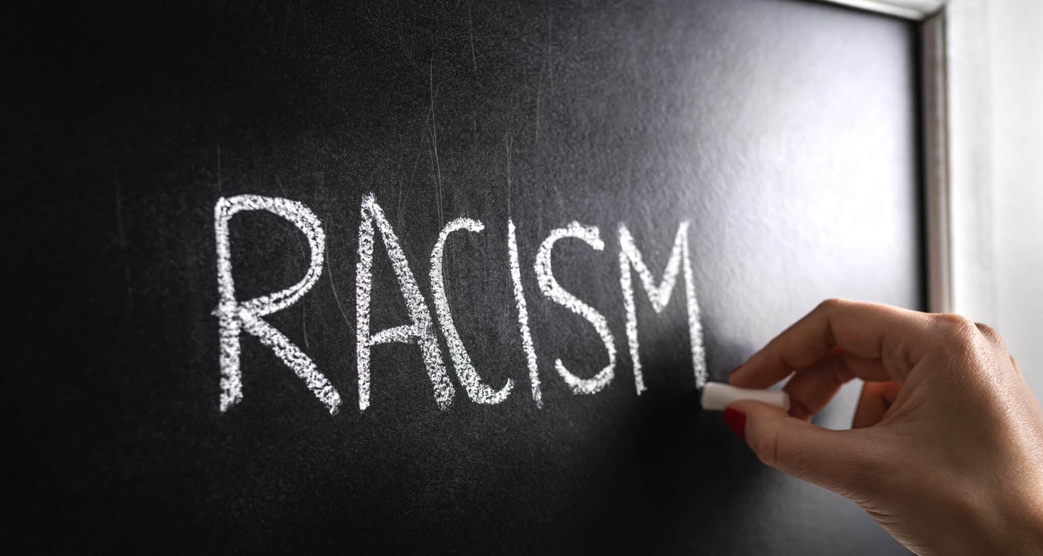 Hand writing the word racism on blackboard, racist