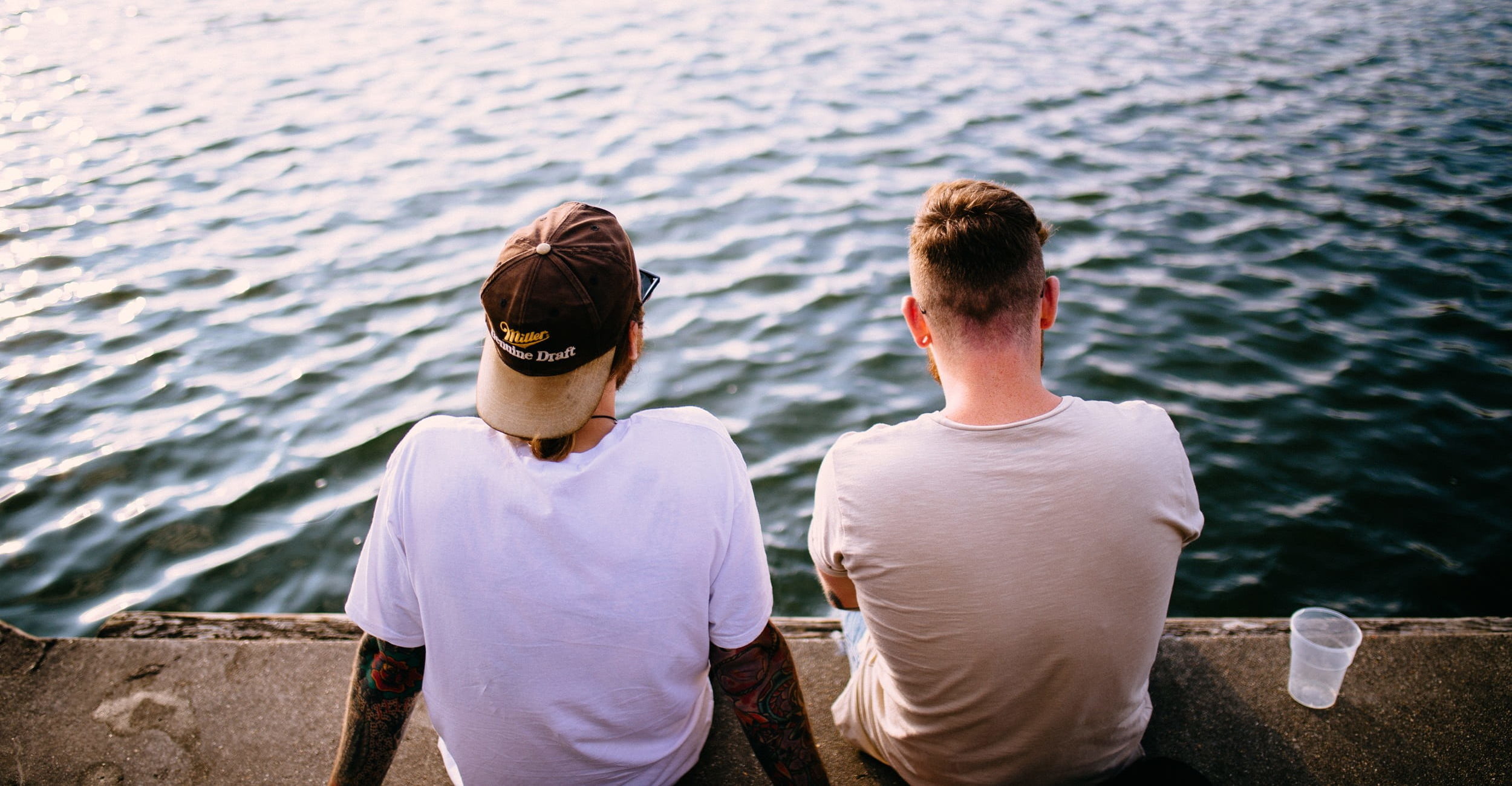 two men sitting by river picture from back