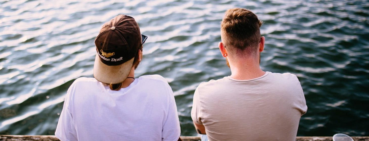 two men sitting at river picture from the back