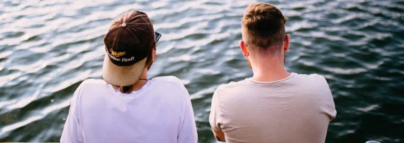 two men sitting at river picture from the back