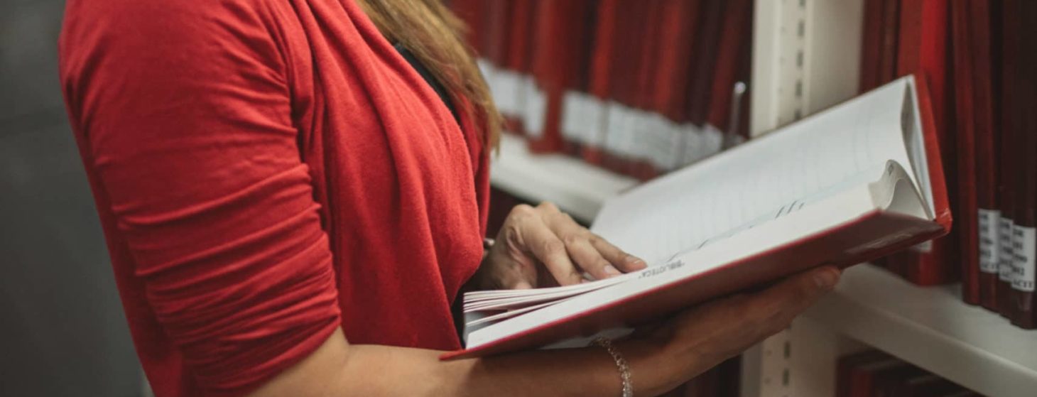 woman reading book standing in library