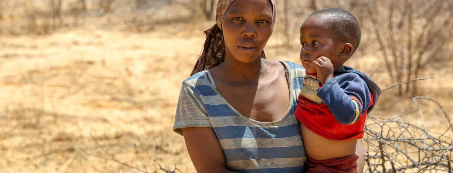 African woman with a child in a village in Botswana standing in front of the bush in Kalahari , Botswana