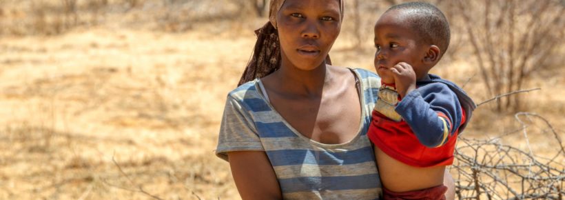 African woman with a child in a village in Botswana standing in front of the bush in Kalahari , Botswana