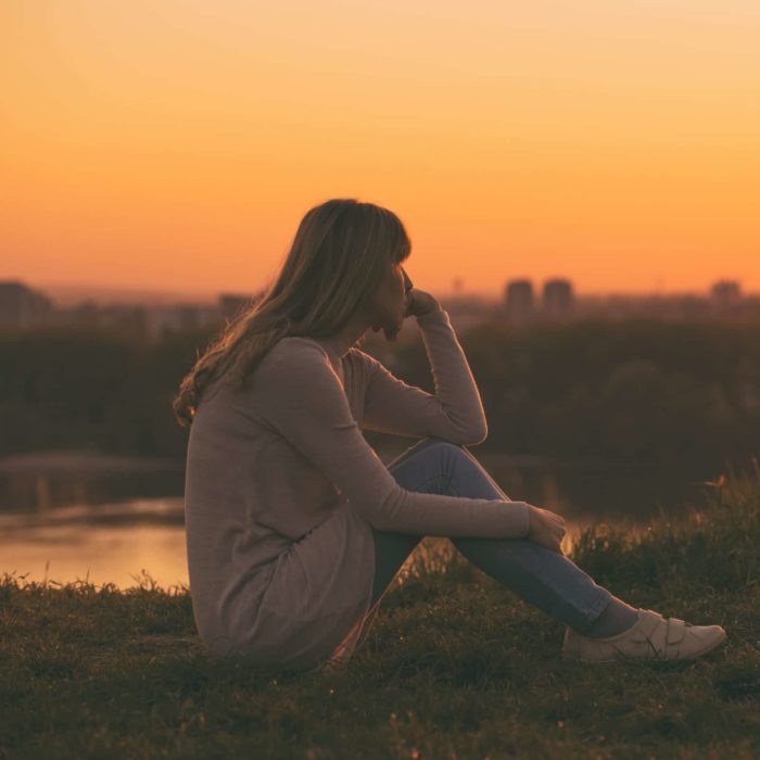 Sad woman sitting at the sunset and thinking.