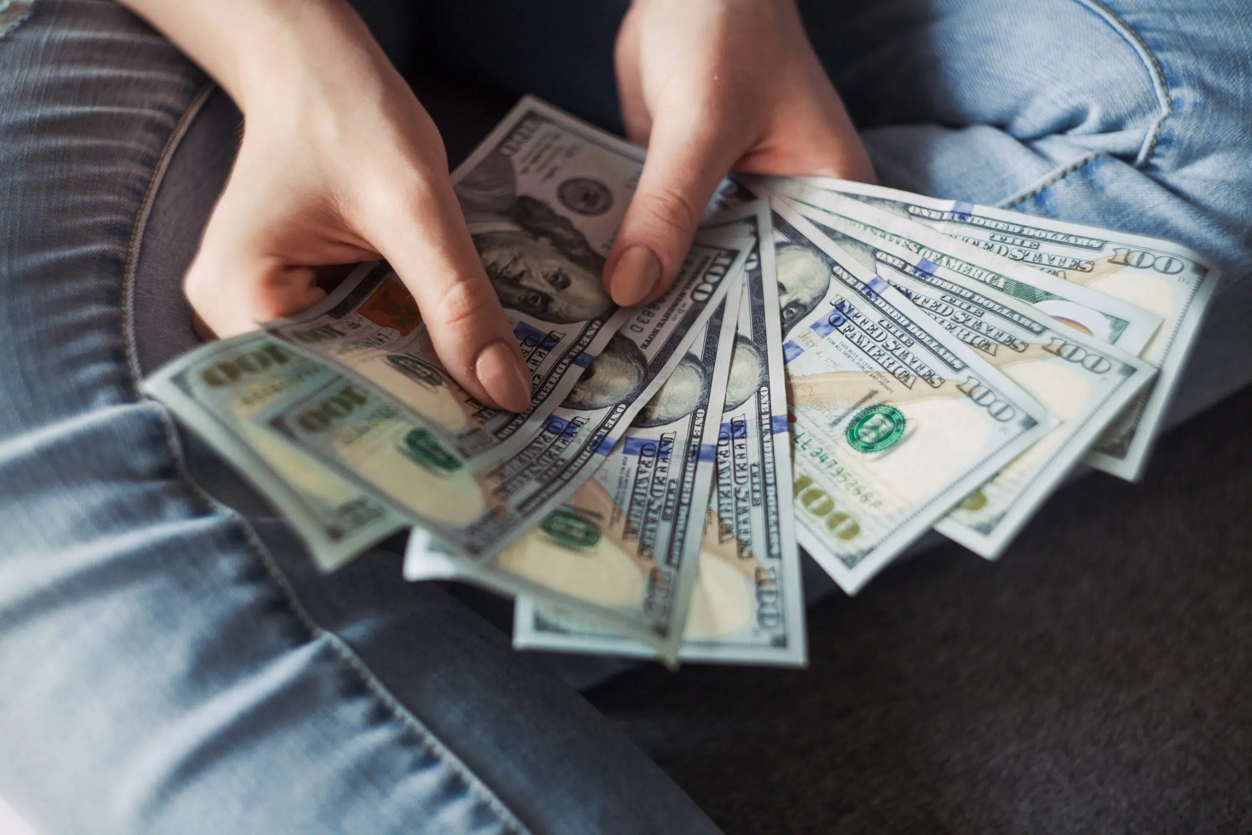 person fanning hundred dollar bills with his hands sitting down