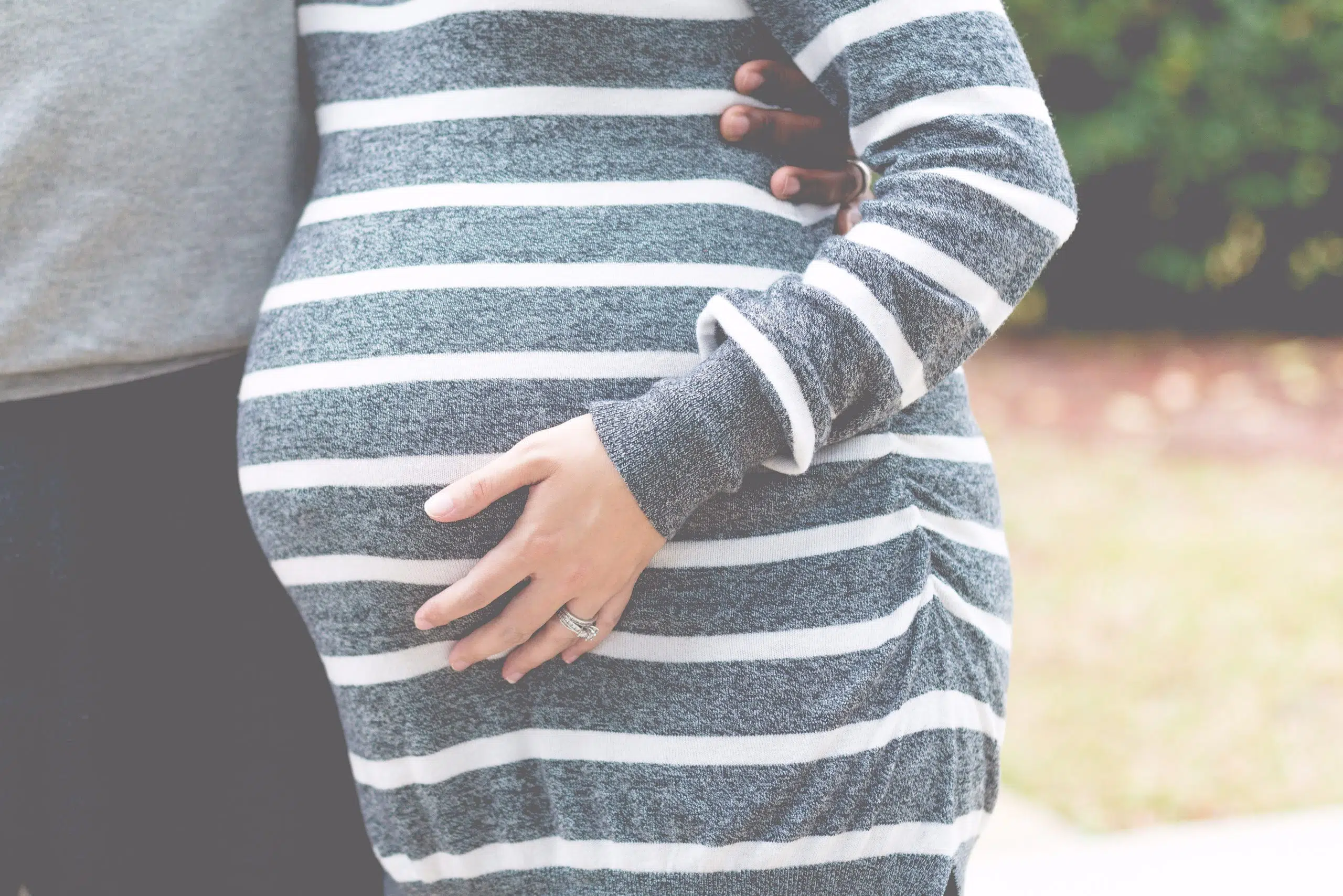 pregnant woman in striped dress with man's arm around her waste