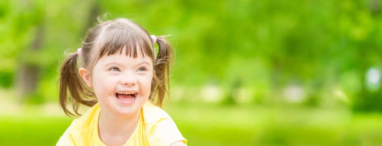 Portrait of a joyful little girl with syndrome down in a summer park