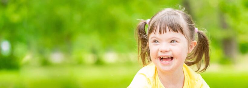 Portrait of a joyful little girl with syndrome down in a summer park