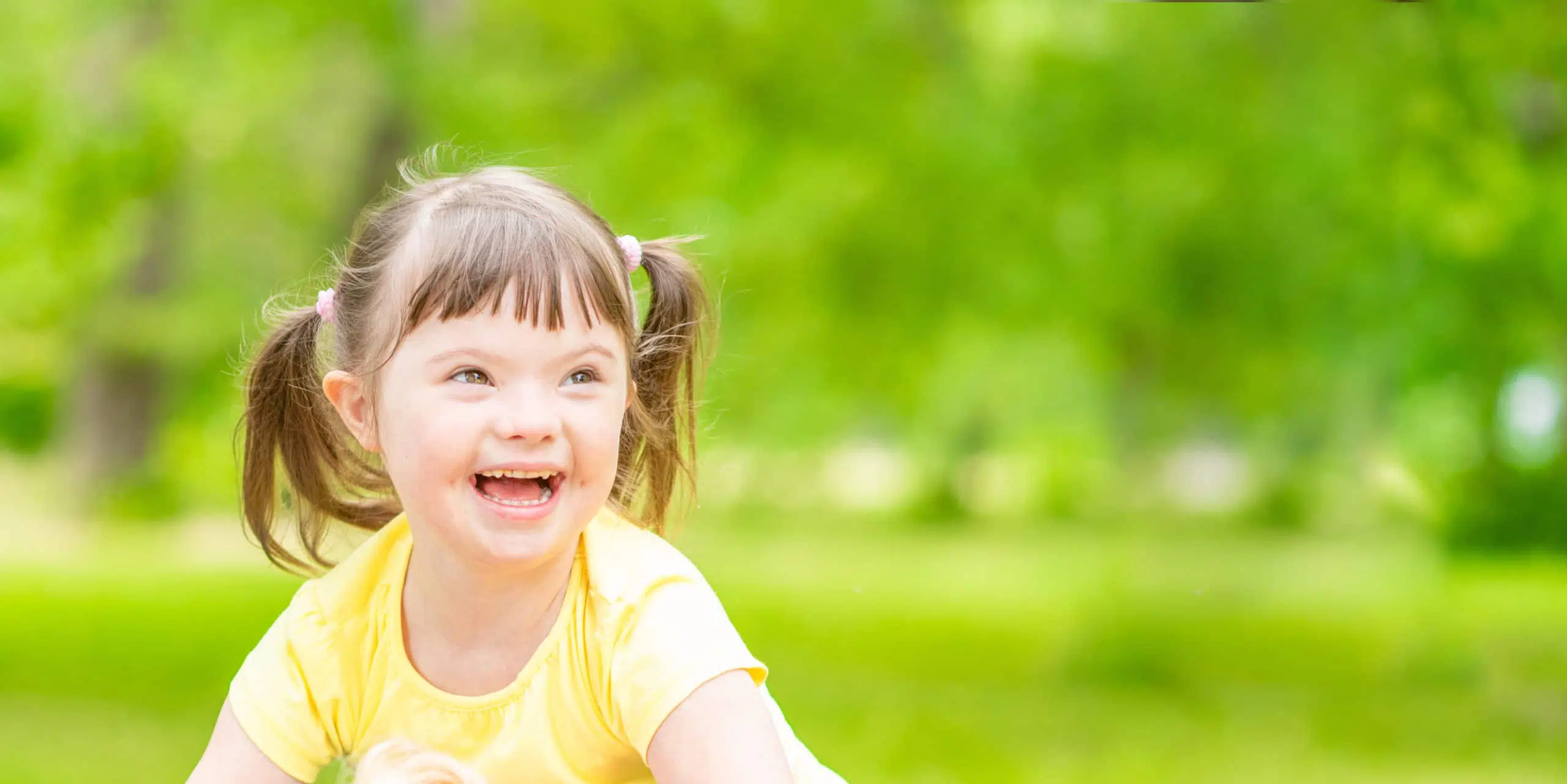 Portrait of a joyful little girl with syndrome down in a summer park