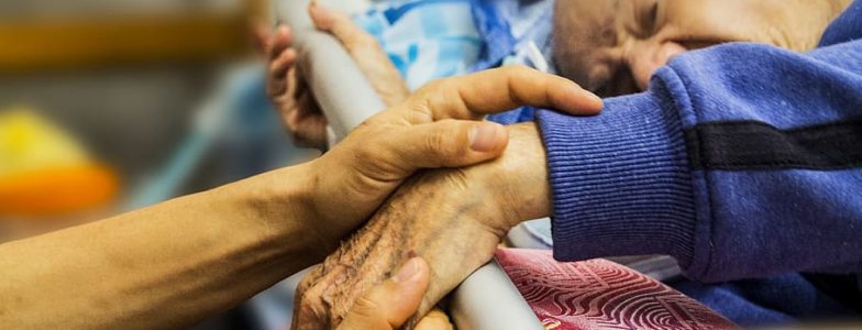 elderly man in bed with someone taking care of him