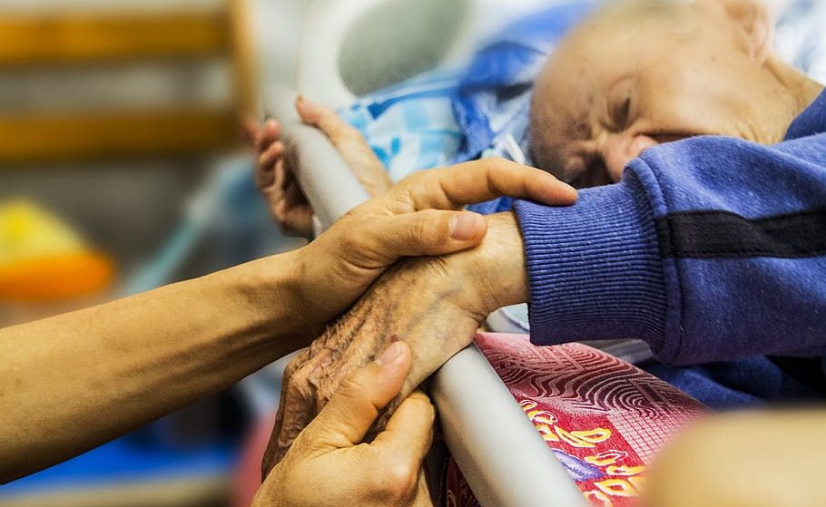 elderly man in bed with someone taking care of him