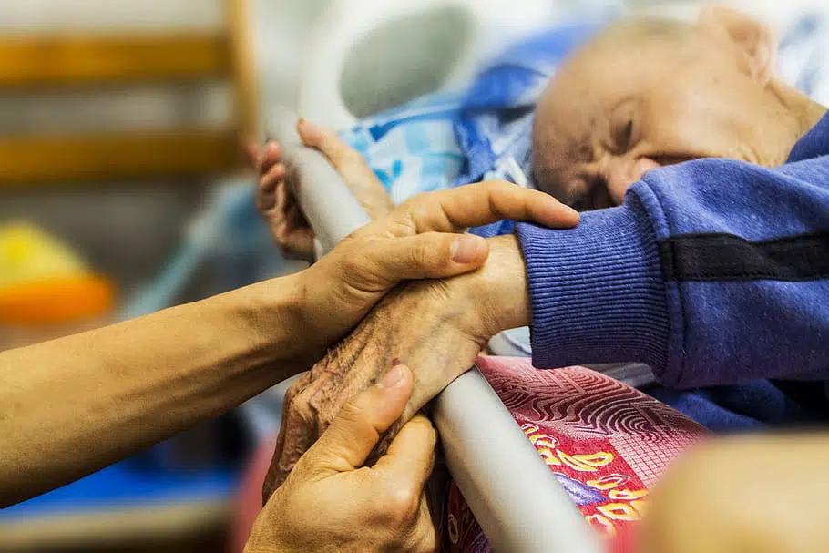 elderly man in bed with someone taking care of him