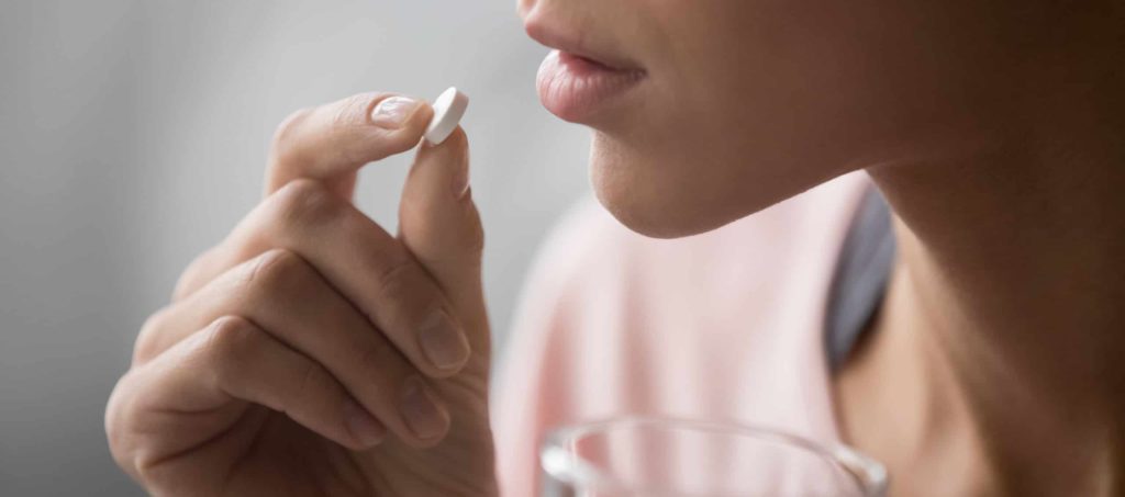 woman taking a pill and holding a glass of water