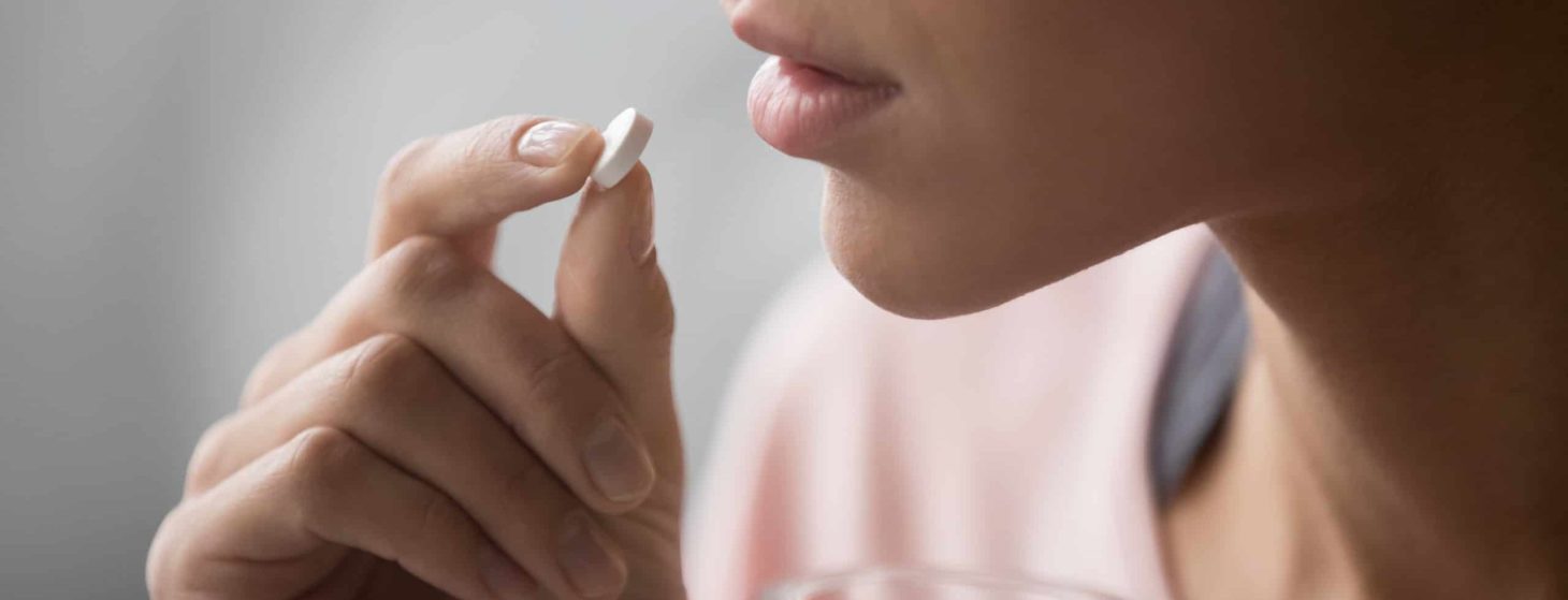 woman taking a pill and holding a glass of water