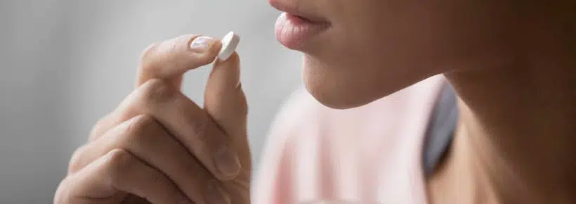 woman taking a pill and holding a glass of water