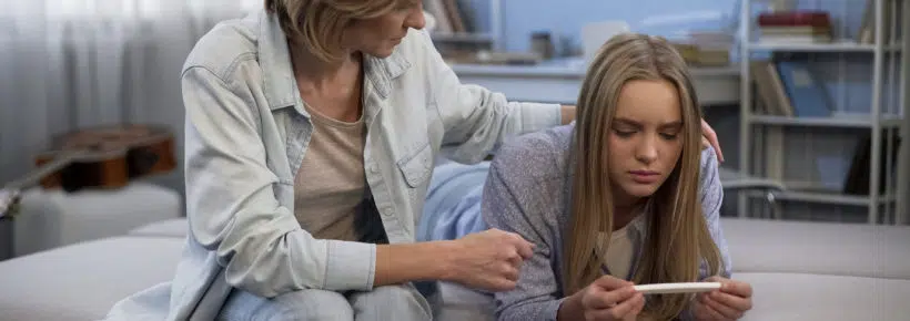 Sad teenager looking at positive pregnancy test, mother supporting daughter