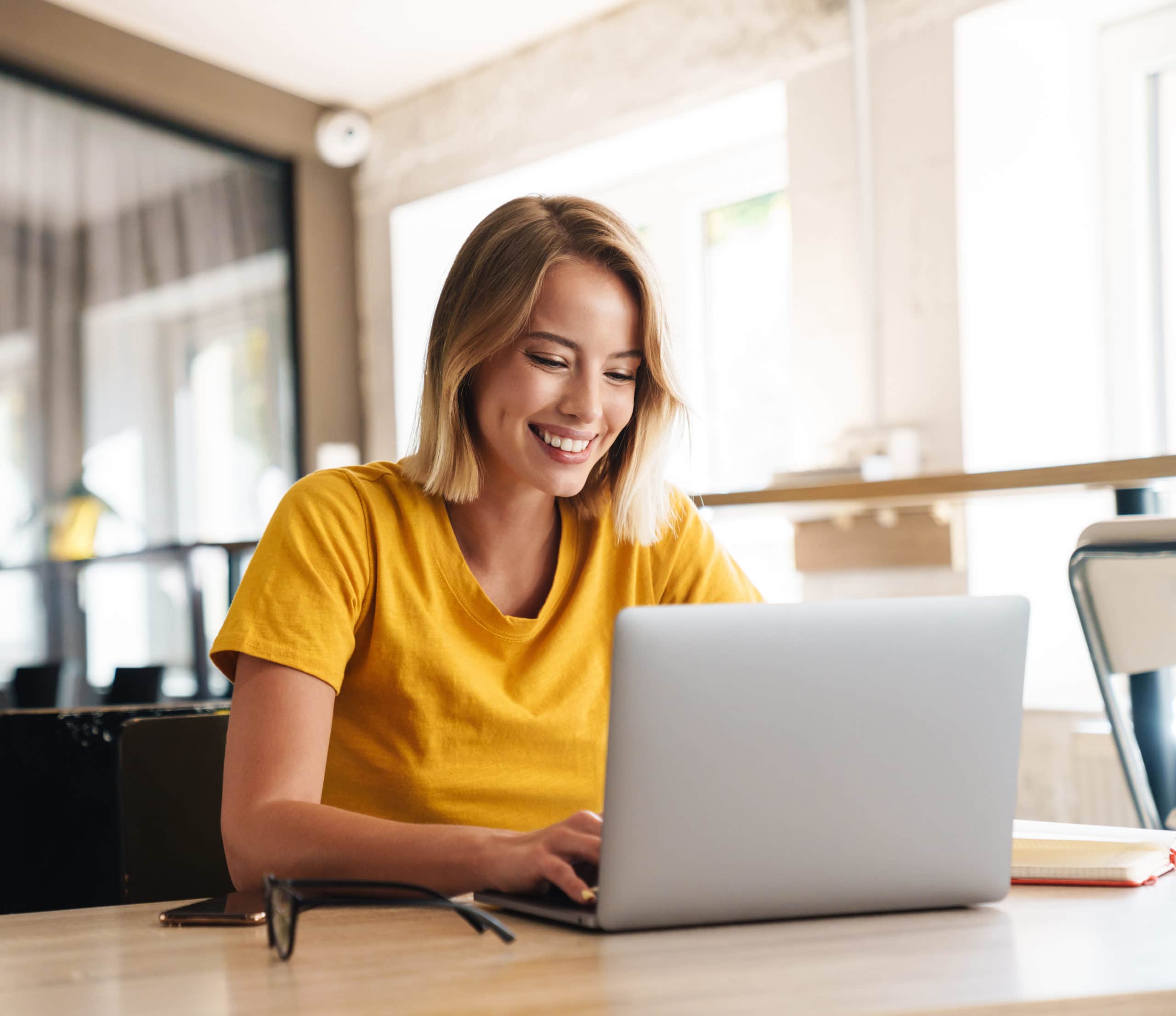 Photo of joyful nice woman using laptop and smiling while sitting at table in open-plan office