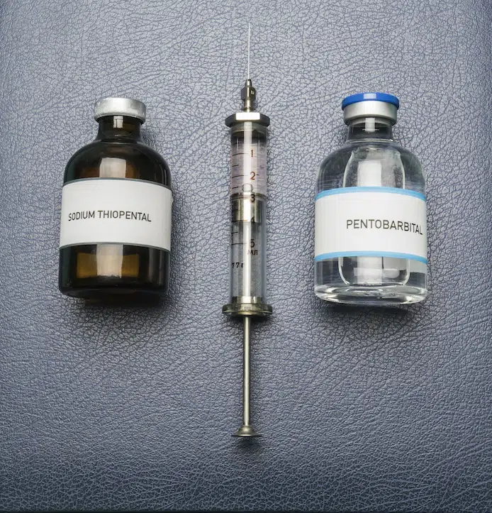 Vintage syringe and drugs used in lethal injection on a book of euthanasia, digital composition, conceptual image