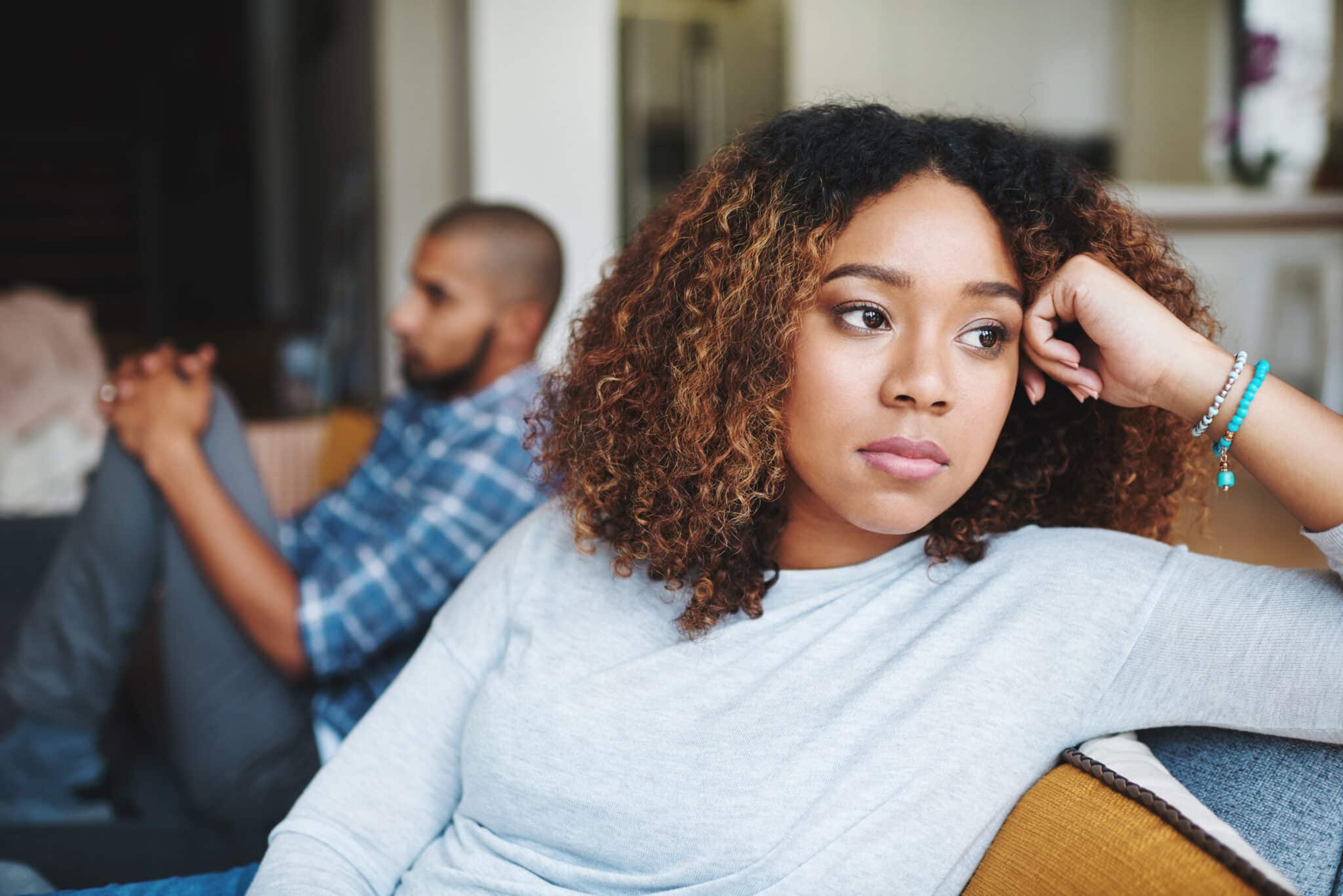 Unhappy couple and sad woman upset after argument or conflict with her man on home sofa. Angry girlfriend or female thinking about disagreement or ignoring partner, tired of relationship problems