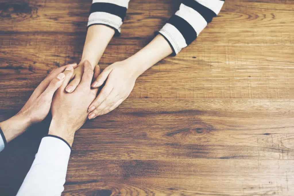 Close up on a man and a woman holding hands at a wooden table