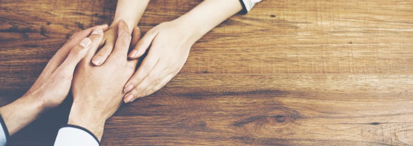 Close up on a man and a woman holding hands at a wooden table