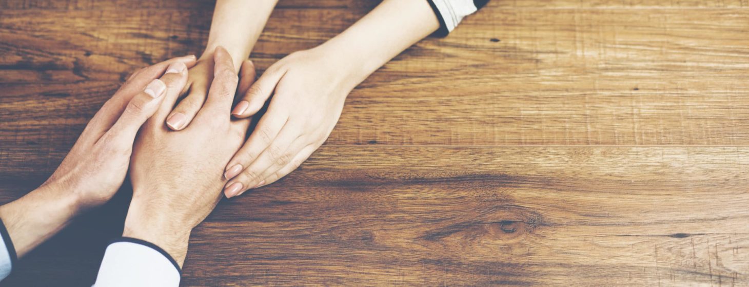 Close up on a man and a woman holding hands at a wooden table