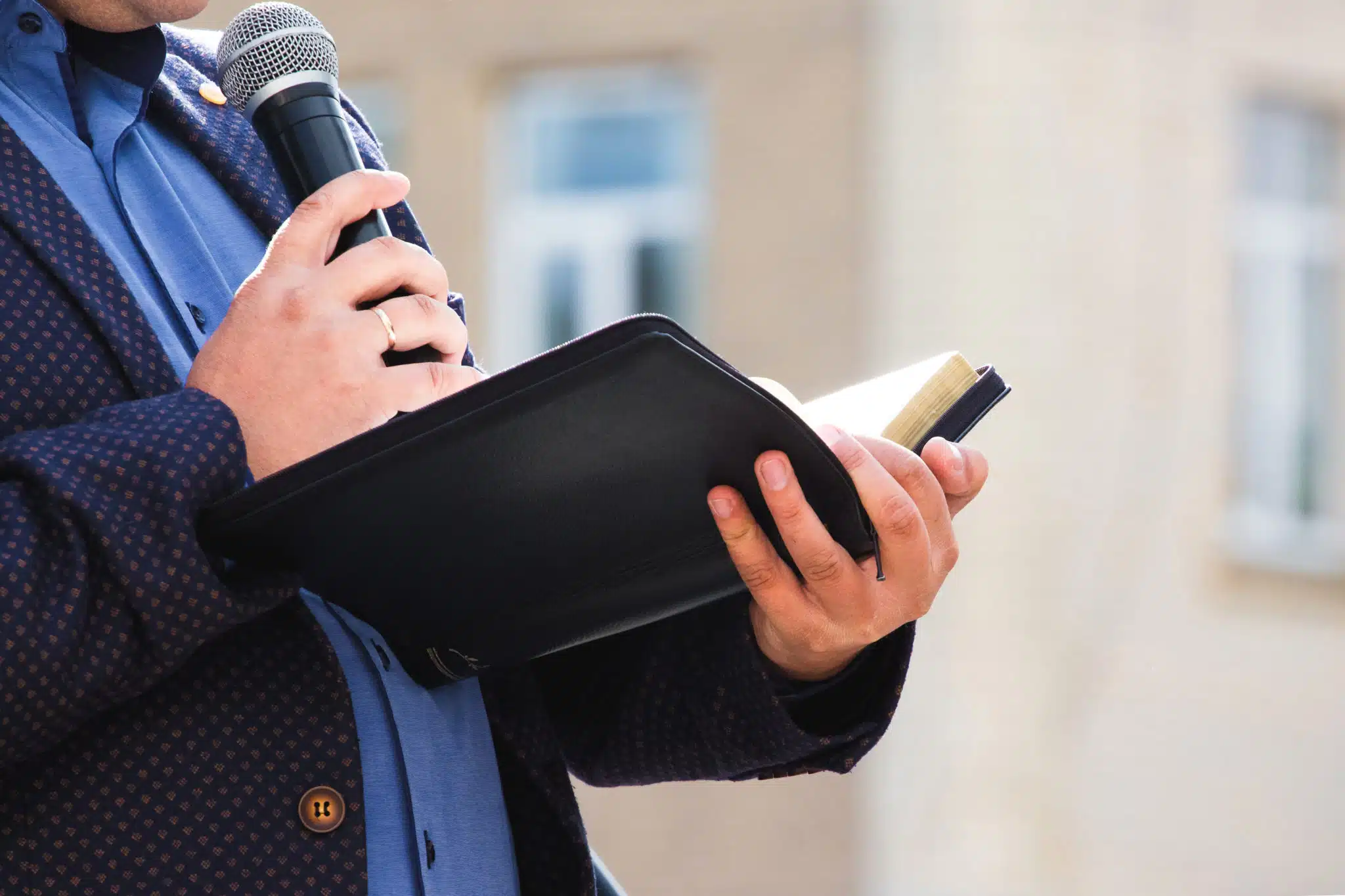 A preacher with a microphone in his hand holds a Bible and reads - what does the bible say about transgender