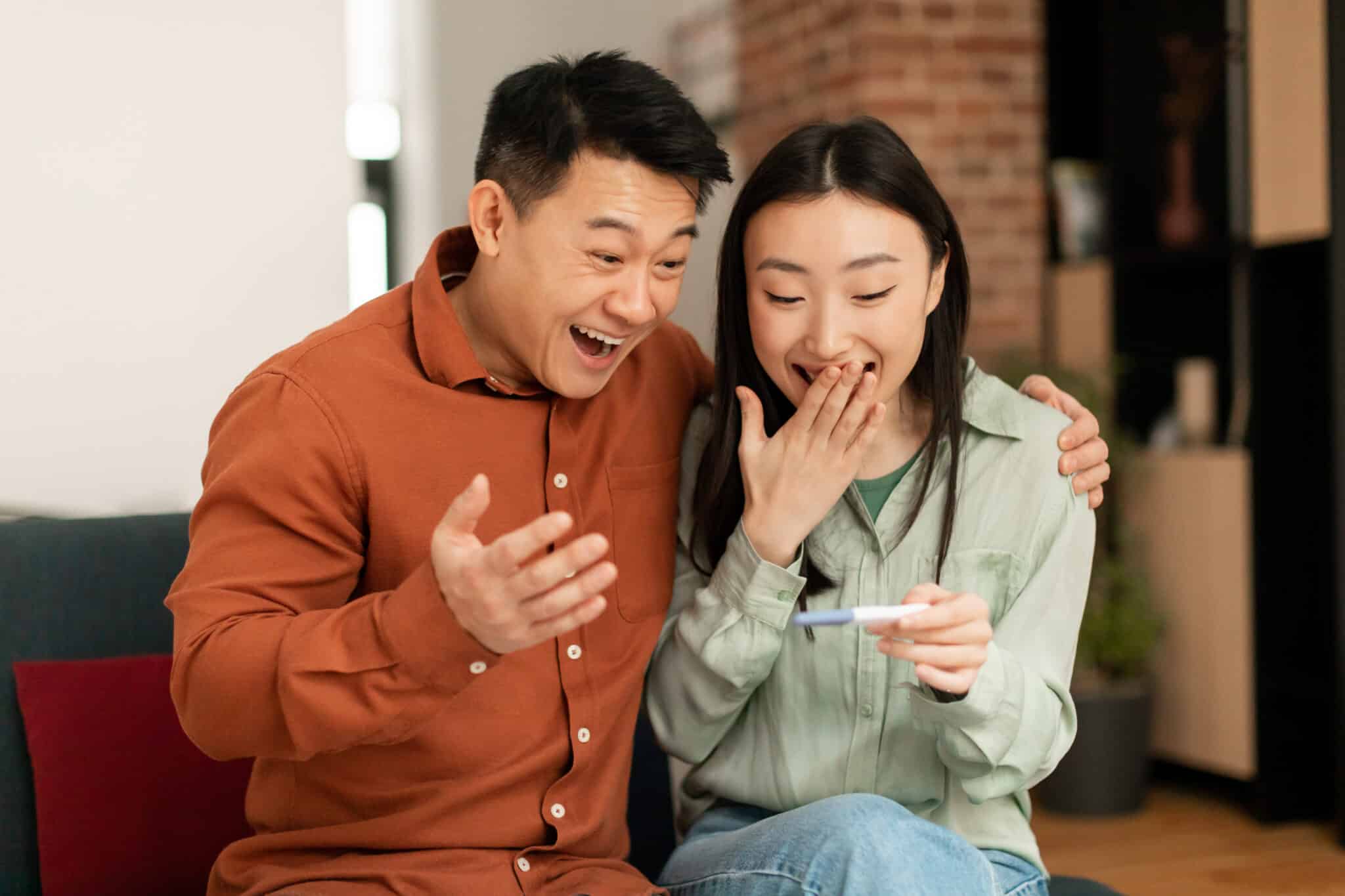 excited expecting Japanese couple looking at a positive pregnancy test