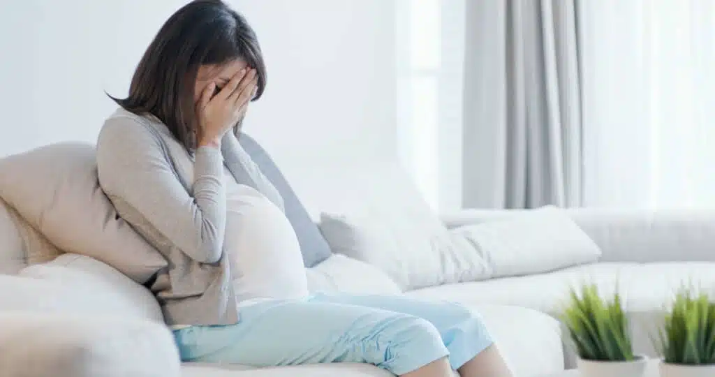 sad pregnant woman sitting on sofa