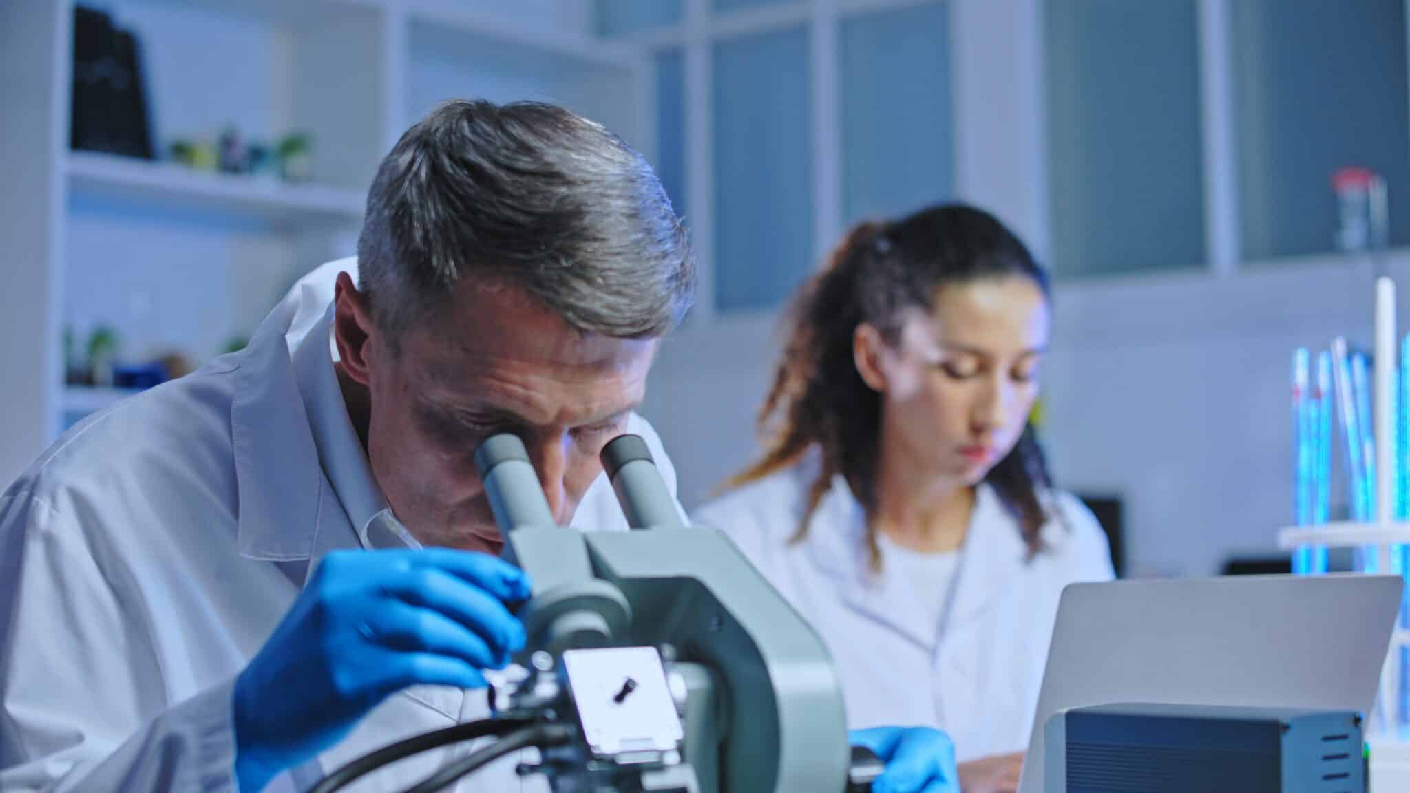 Oncology doctor examining tissue sample under microscope, clinic