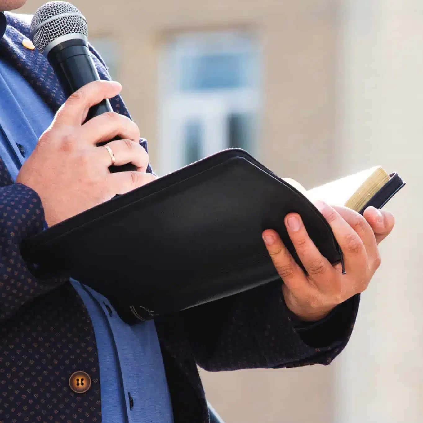 A preacher with a microphone in his hand holds a Bible and reads a passage from it
