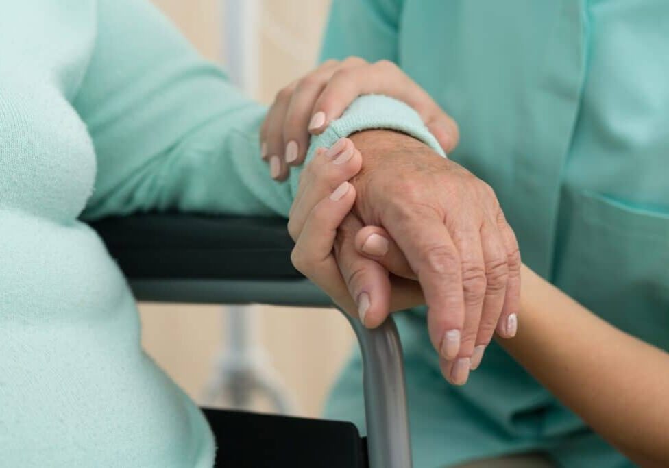 Photo of nurse supporting old woman on wheelchair
